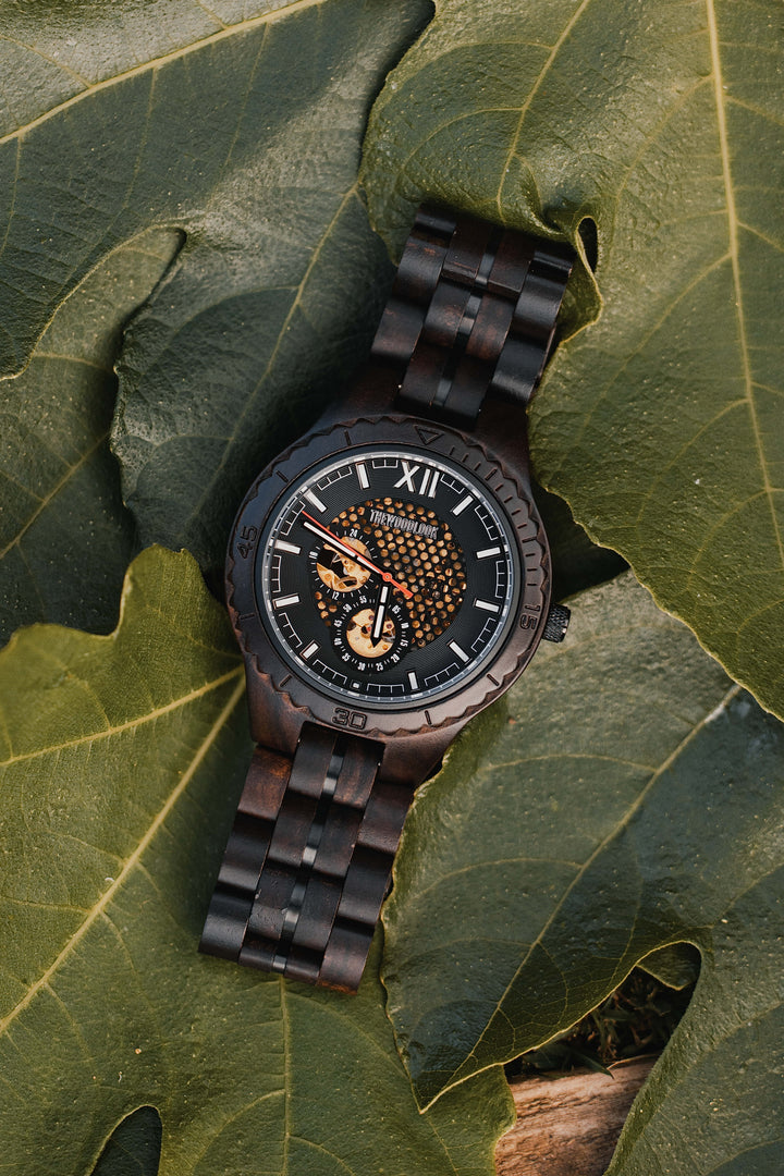 Detroit ebony mechanical wooden watch lying on large green leaves - The Wood Look