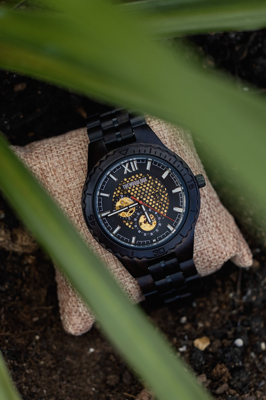 Detroit ebony mechanical wooden watch on a cushion, seen through green leaves - The Wood Look