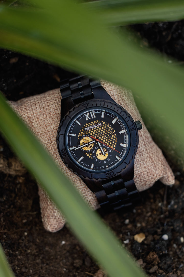 Detroit ebony mechanical wooden watch on a cushion, seen through green leaves - The Wood Look
