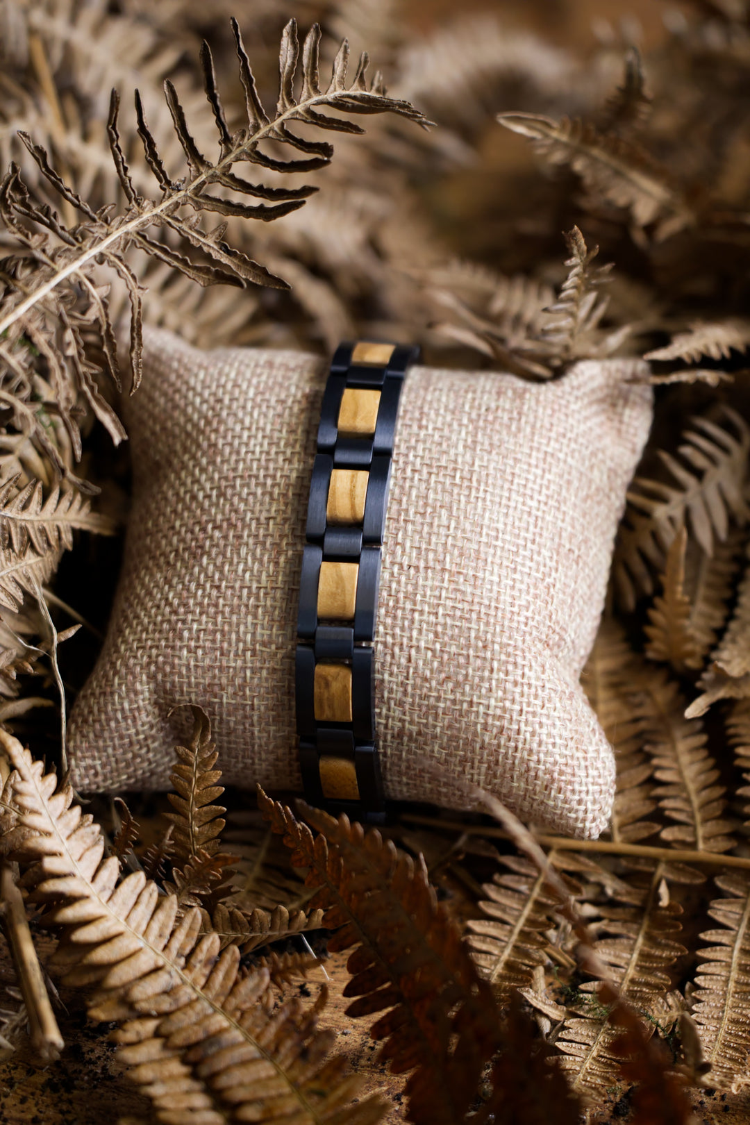 Paracas olive wood and black steel bracelet on a cushion among dried ferns - The Wood Look
