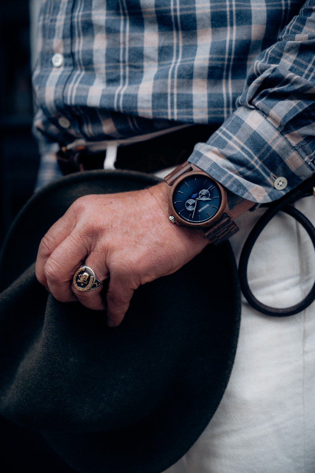 Man in a check shirt wearing the Goa walnut wooden watch while holding a hat - The Wood Look
